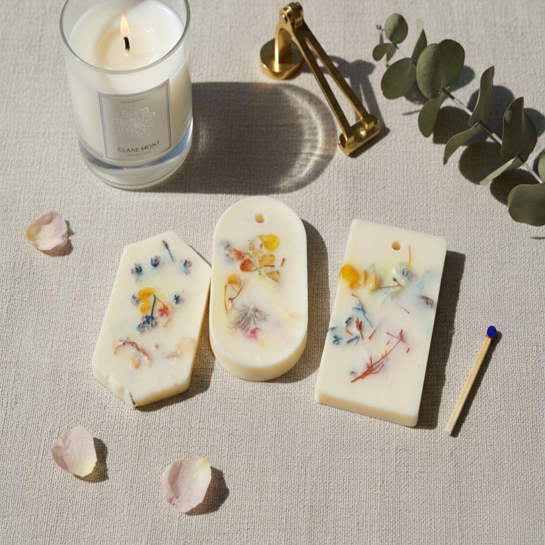 Three handmade aroma tags bars with floral designs next to a candle on a textured surface. For hanging to increase fragrance in your home.