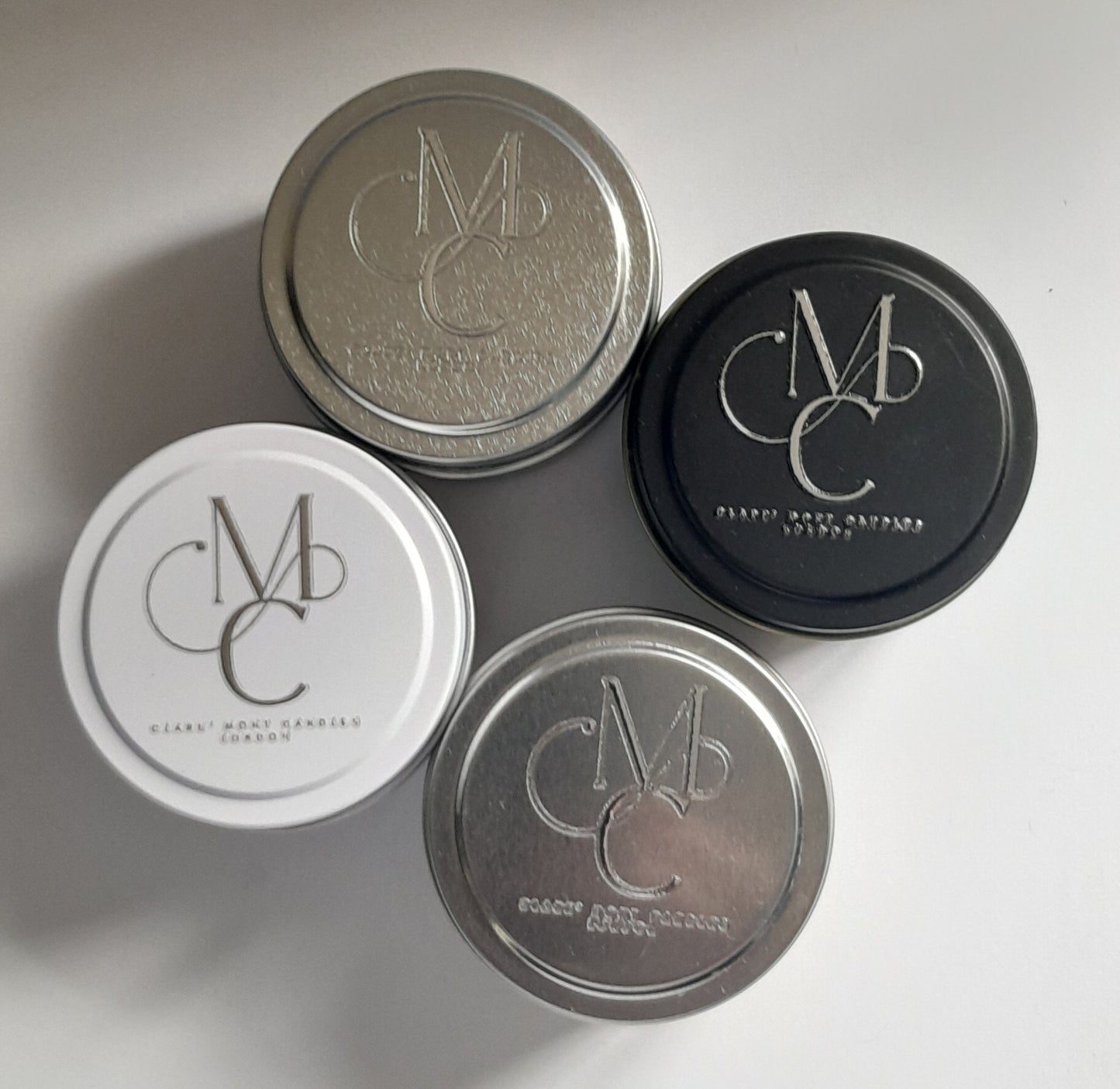 Four candle tins with 'CMC' logo on lids against a white background