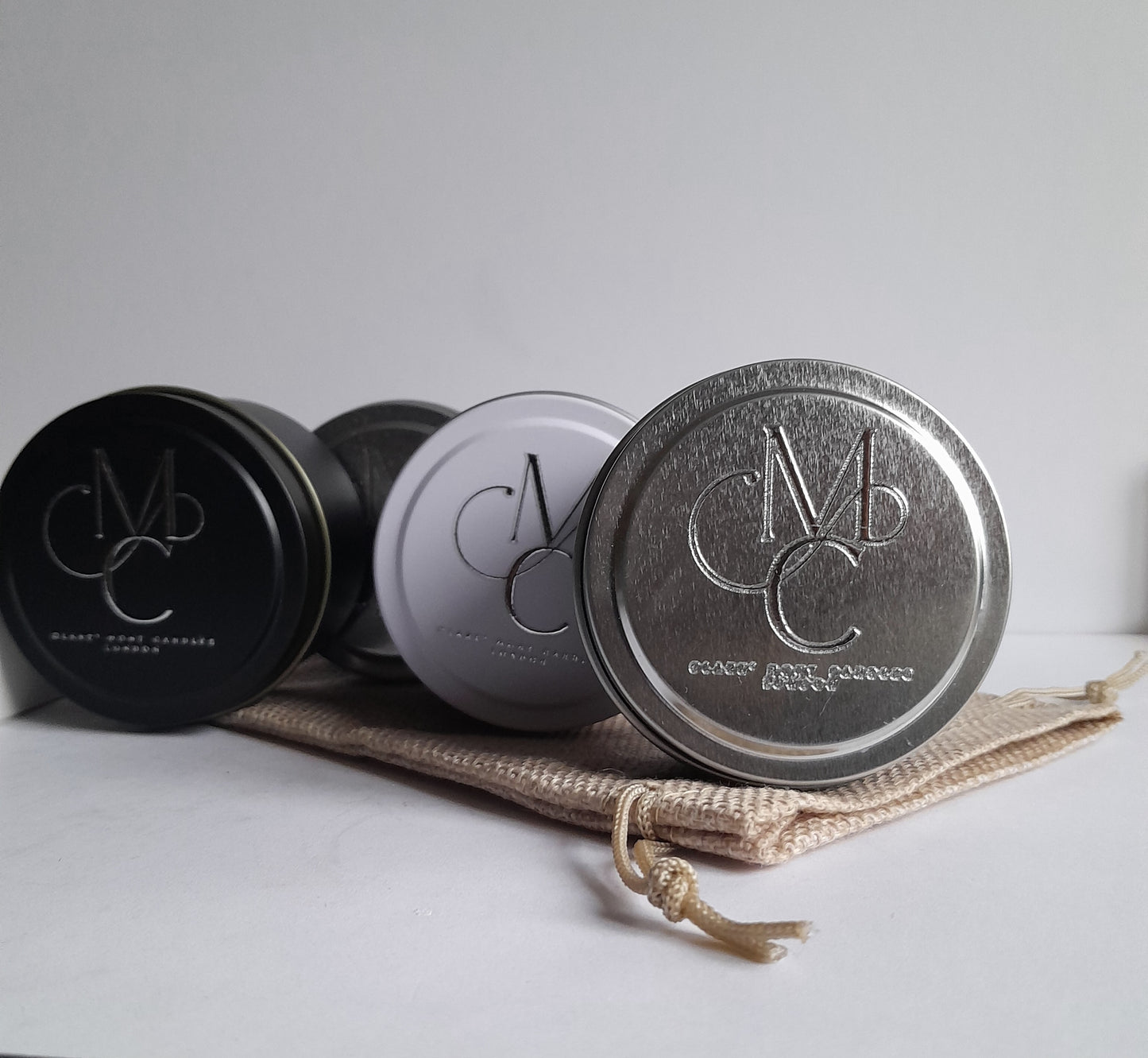 Three Clare` Mont Candle tins with a logo on a white surface
