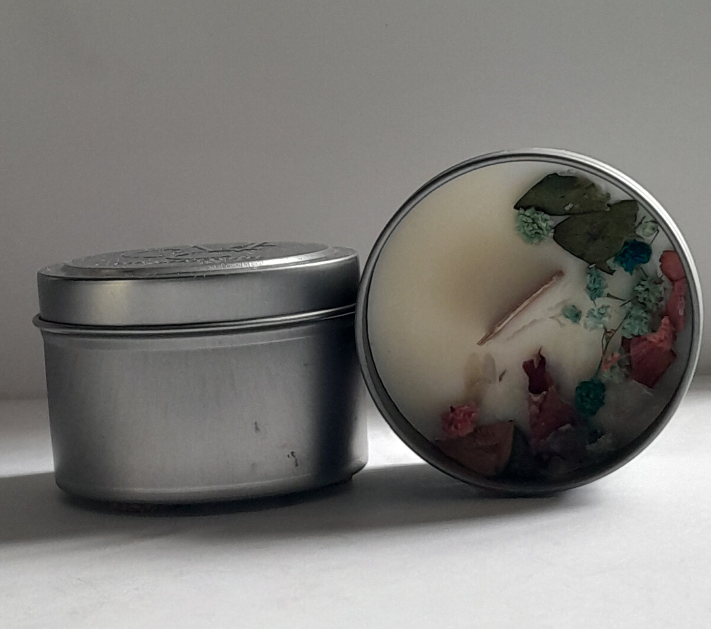 Silver tin with a decorated lid featuring floral and nature-themed design on a neutral background