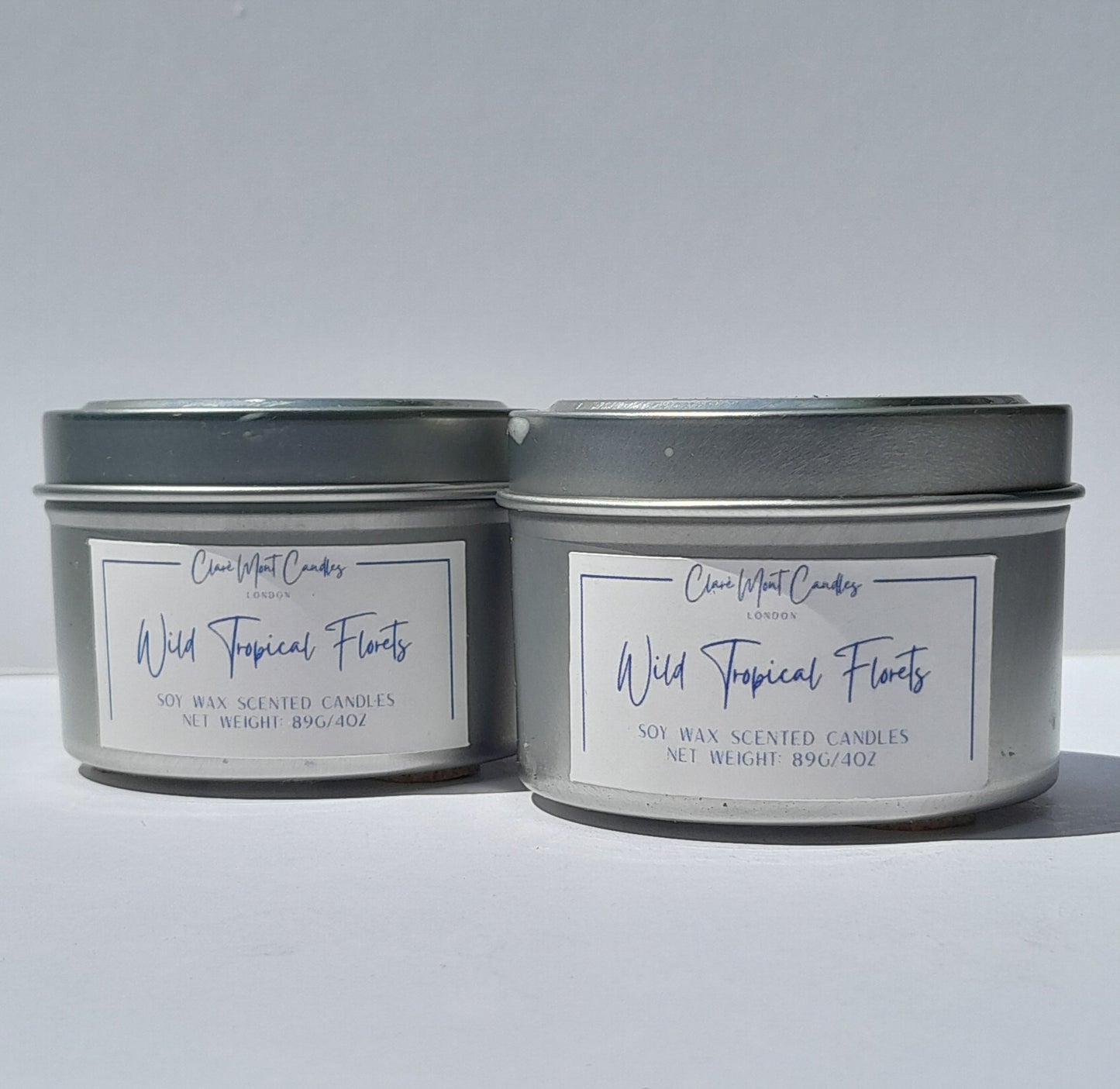 Two tins of 'Wild Tropical Florals' candles side by side with labels on a white background