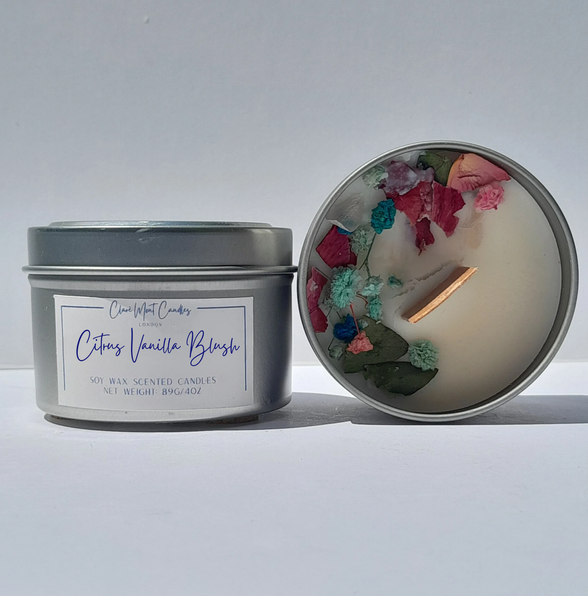 Candle in a tin with floral elements and visible label on a white background