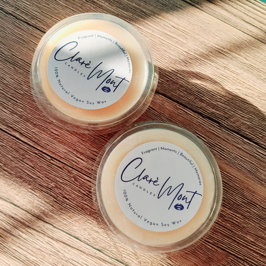 Two round wax melt inserts on a wooden surface, with 'Clare Mint' branding and a description of '100% Natural Vegan Soy Wax' visible on the labels.