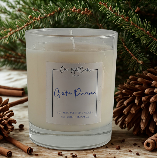 Scented candle labeled 'Golden Pinecone' with pine cones and cinnamon stick decorations in the background