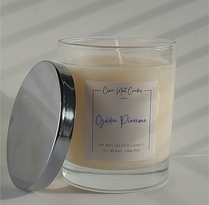 Glass candle with a metal lid labeled 'Golden Pinecone' on a neutral background