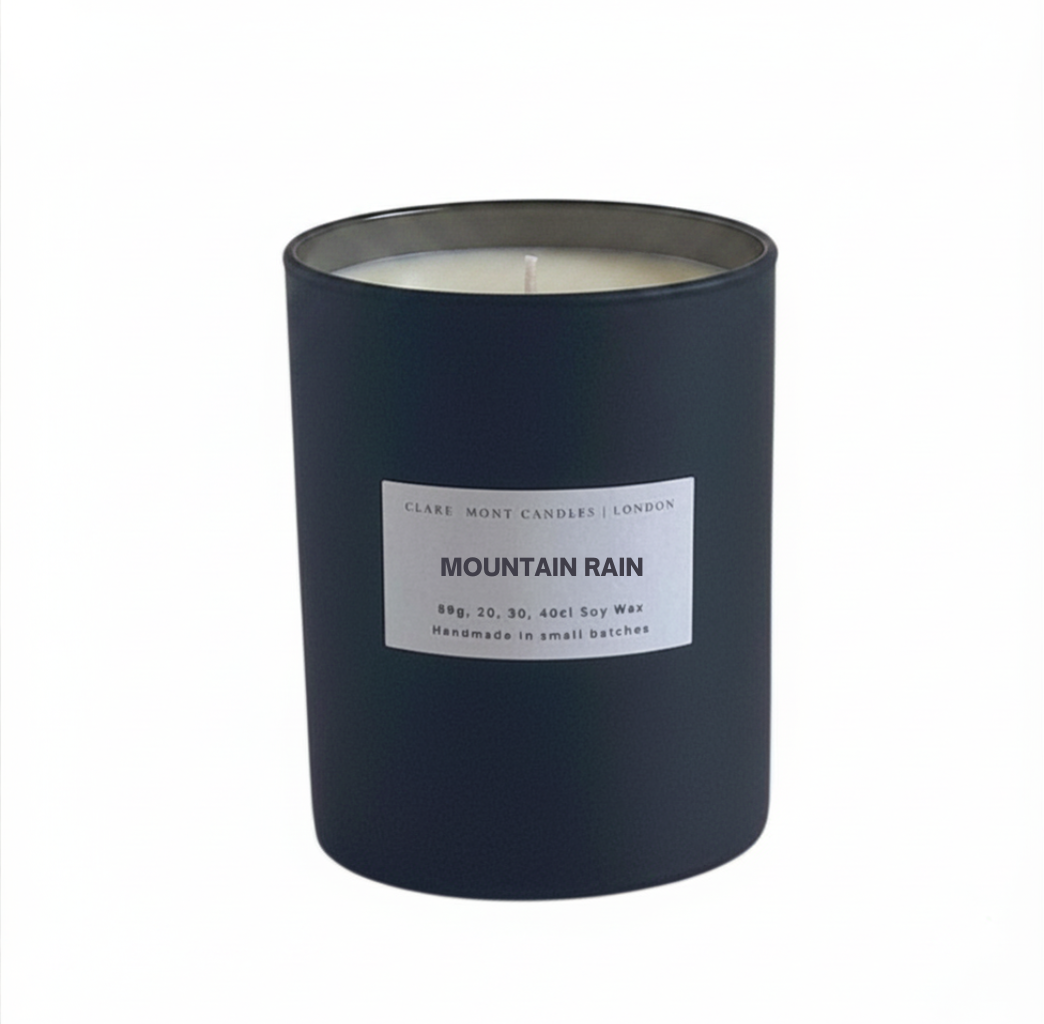 Candle in a dark container labeled 'Mountain Rain' on a white background