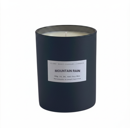 Candle in a dark container labeled 'Mountain Rain' on a white background