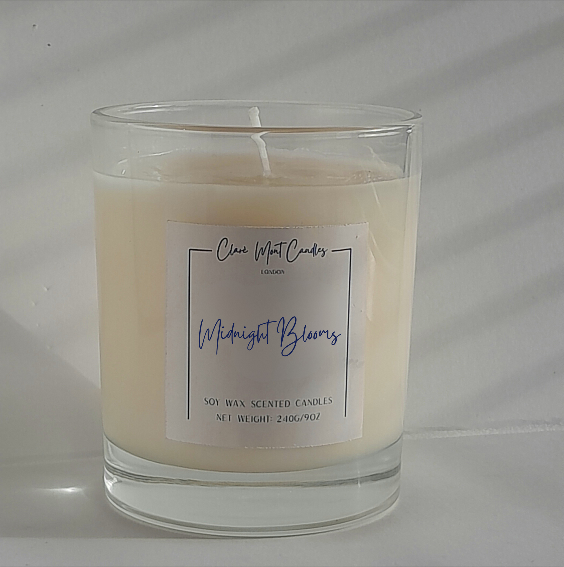 Midnight Blooms candle in clear glass near gardenia petals and soft lighting on a bedside table.
