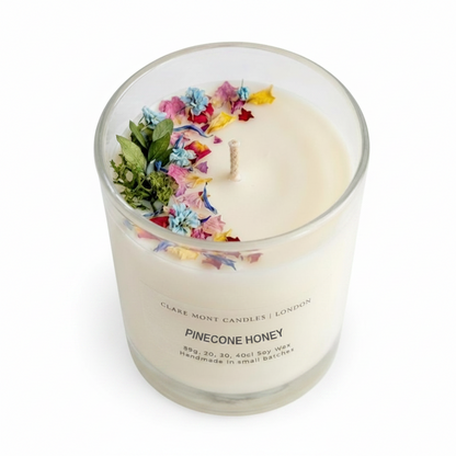 Pinecone Honey hand poured Clare' Mont Candle with colourful flowers and leaves in a glass container on a white background