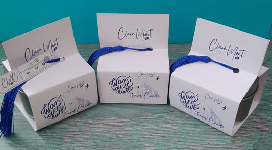 Three boxes of Wanderlust  travel candles on a wooden surface with a teal background.