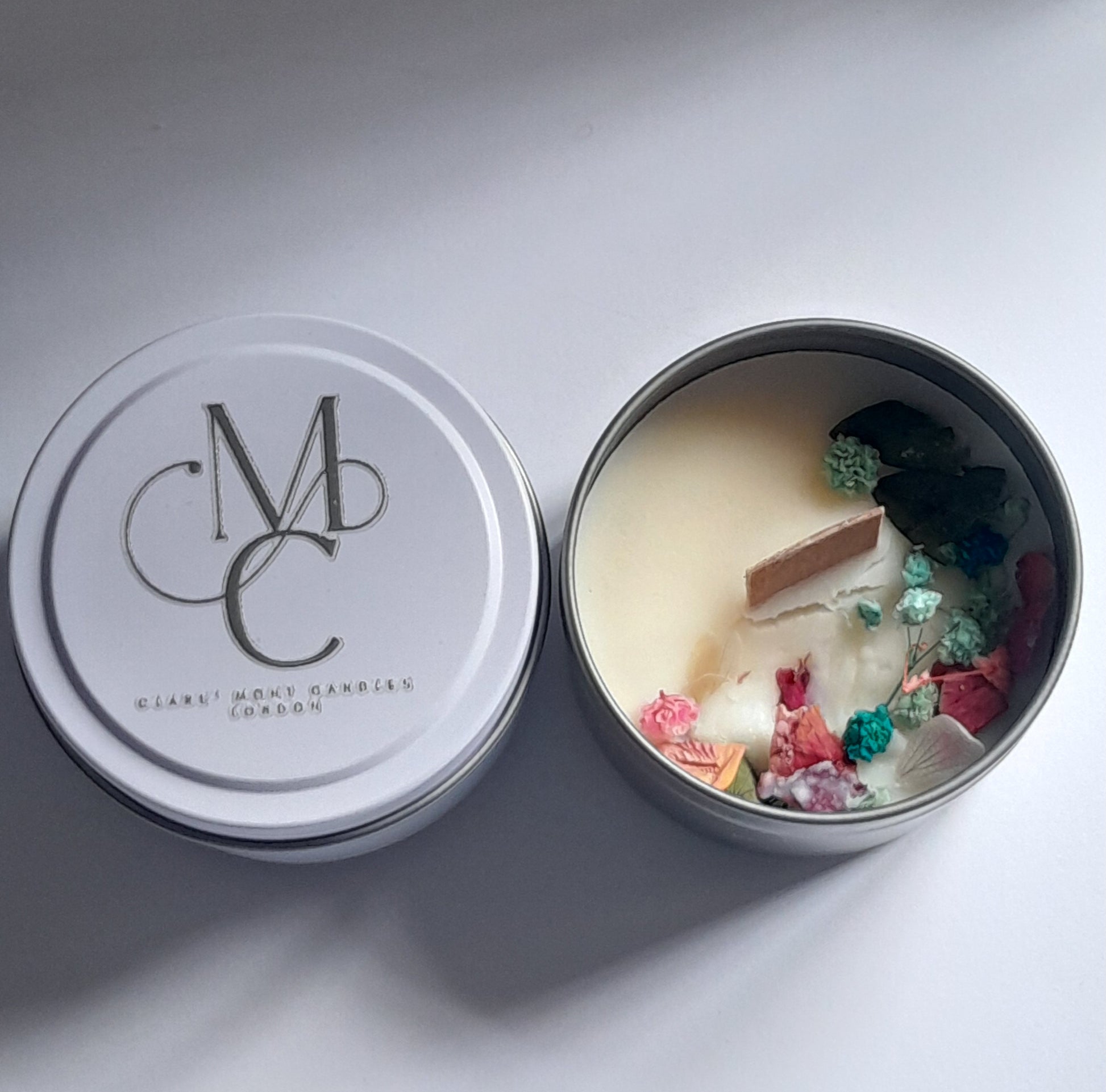 Candle in a tin with colorful decorative elements on a light gray background