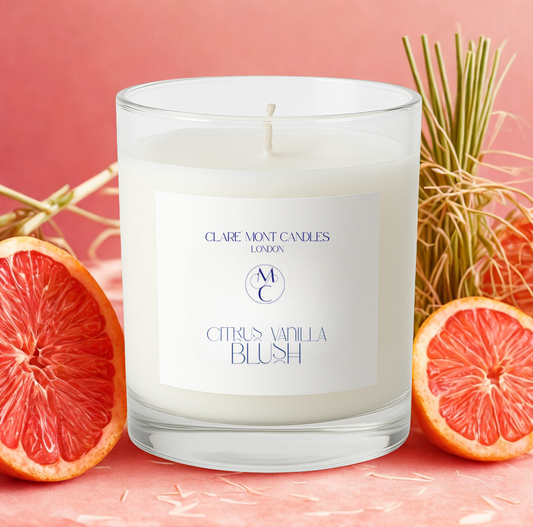 Candle with a label in front of grapefruit slices and dried grasses on a pink background