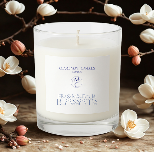 White candle with a label on a wooden surface with flowers in the background